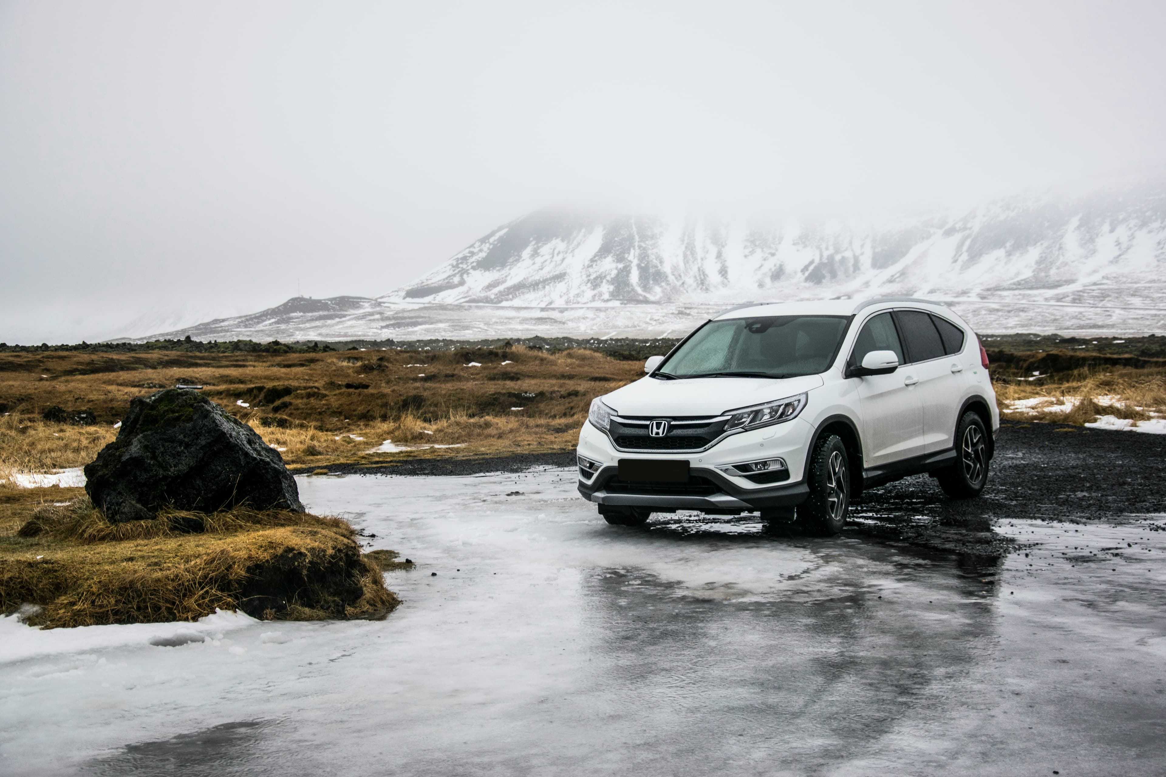 White Honda CR-V rental car parked by an icy roadside with snow-capped mountains in the background