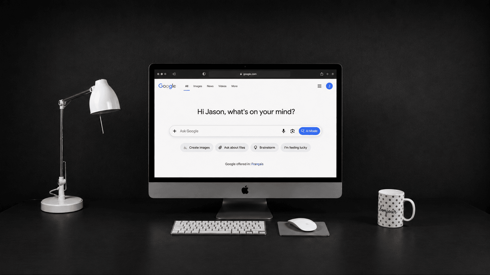 Desktop monitor on a dark desk showing the Google AI Mode home screen with the AI Mode button in the search bar