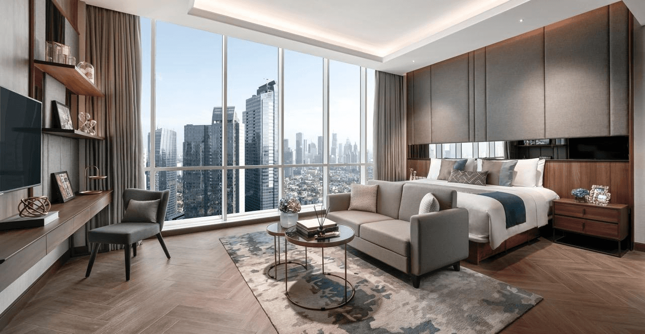 Living area and bedroom of a suite at Oakwood Premier Cozmo Jakarta with floor-to-ceiling windows over the city