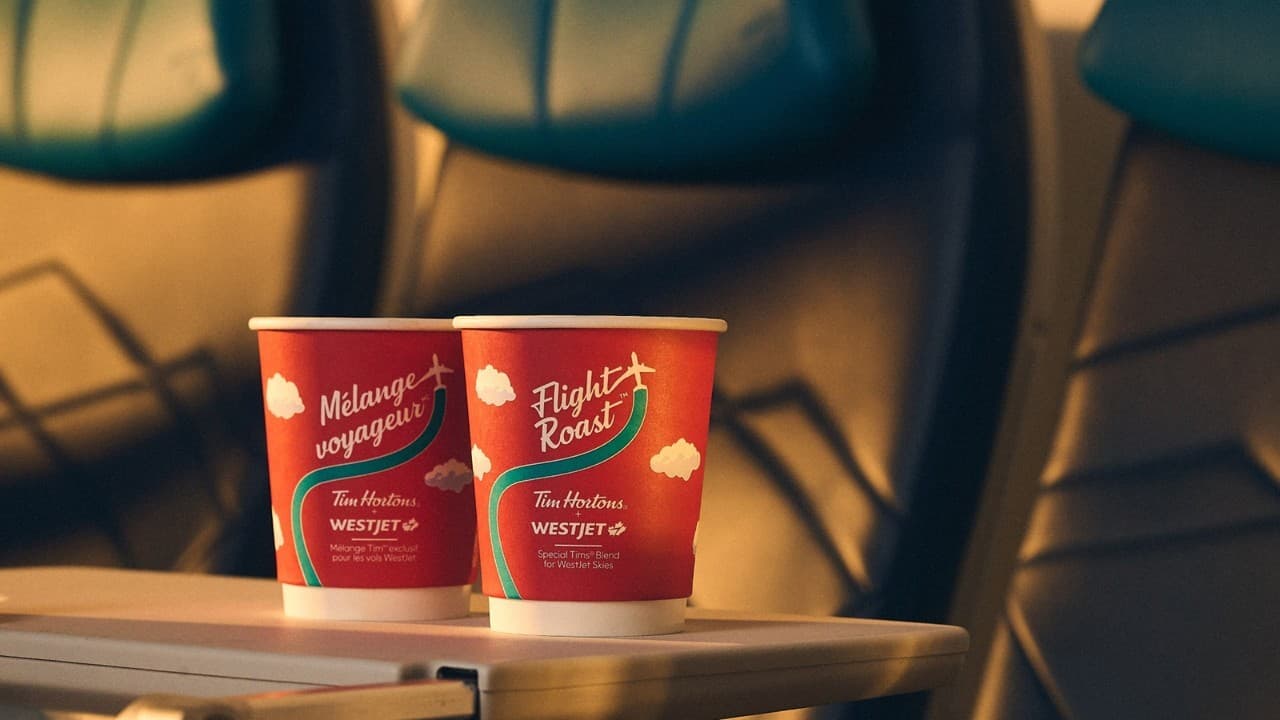Two Tim Hortons Flight Roast cups branded with WestJet on an aircraft tray table