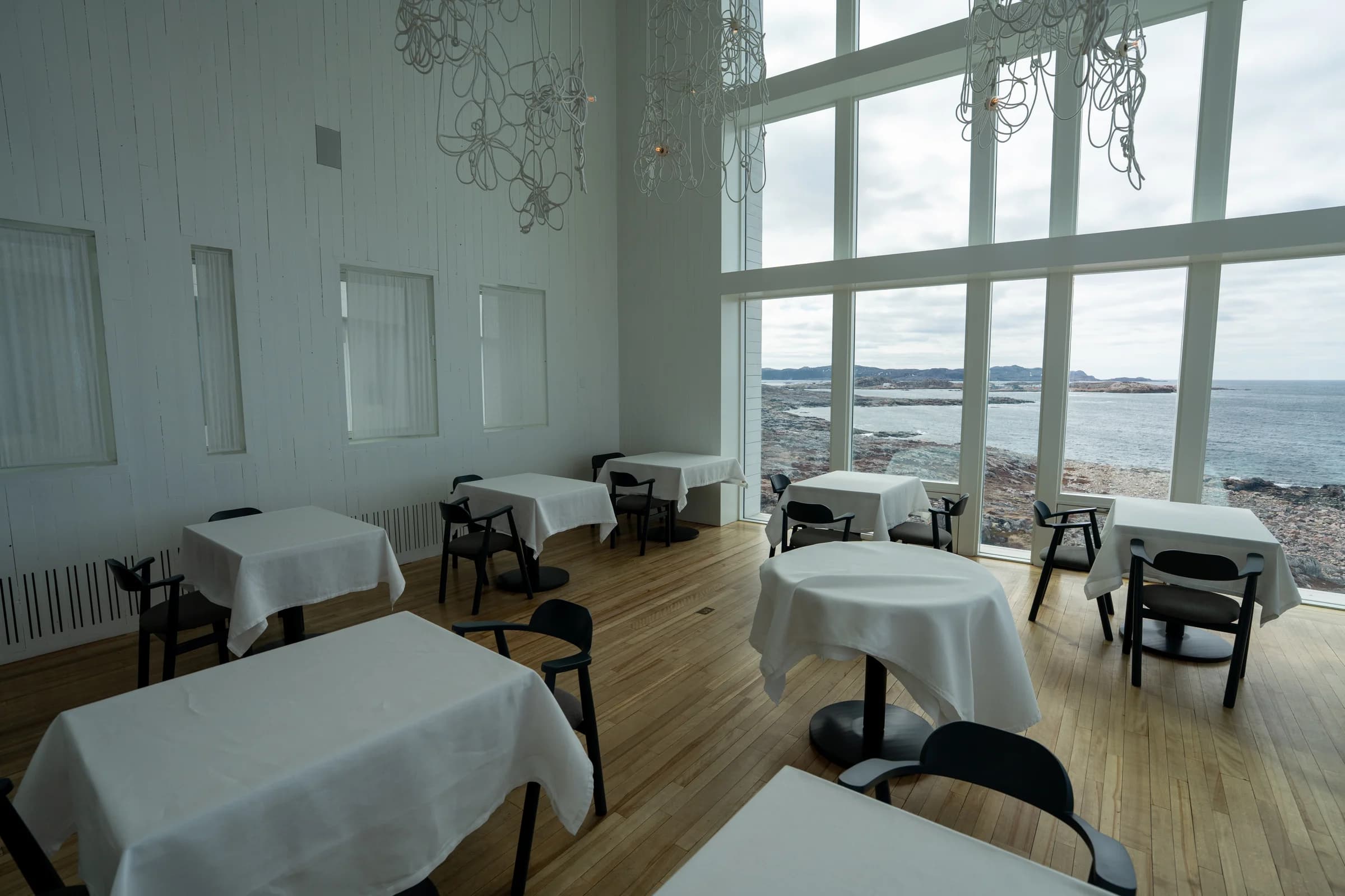 Dining room with white tablecloths and floor-to-ceiling ocean windows at Fogo Island Inn